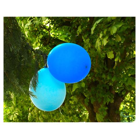 two balloons, one blue and one light blue, floating among green foliage.  The background is filled with lush green leaves, suggesting that the photo was taken outdoors, possibly in a garden or a park. The sunlight filtering through the leaves creates a dappled light effect on the balloons.