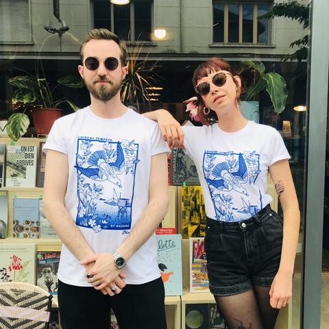 Quentin et Roxanne, les deux libraires à l'origine du projet L'oiseau tempête, posent avec classe : lunettes de soleil, poses décontractées, et teeshirts à l'effigie de l'oiseau tempête sur fond nazairien. On y reconnait une branche de cerisier, une pêcherie, la mer et un porte container en arrière plan. L'illustration est bleue sur teeshirt blanc.