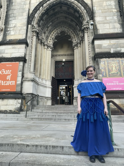 Enby in royal blue eclectic costume on the steps of a cathedral.