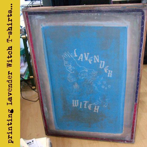 A blue silkscreen is resting upright. It has a design of a goat, a crow, mugwort herbs, stars and the band name Lavender Witch. Text next to it: Printing Lavender Witch shirts".