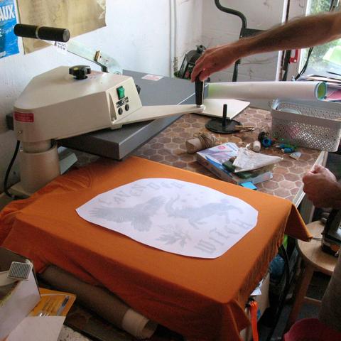 An orange shirt is resting on a hot printing press with a paper on top of it that will transfer the design on the shirt.