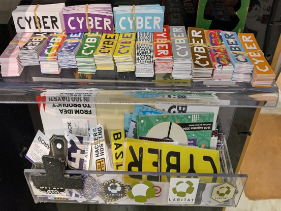 Stickers with the text 'Cyber' in font type OCR-A Bold. They are in a variety of colours and themes placed on top of a small acrylic shelf, which makes a sticker box.