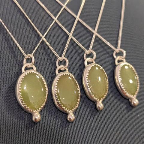 A close-up of four almost identical pendants featuring a jade stone in a silver setting