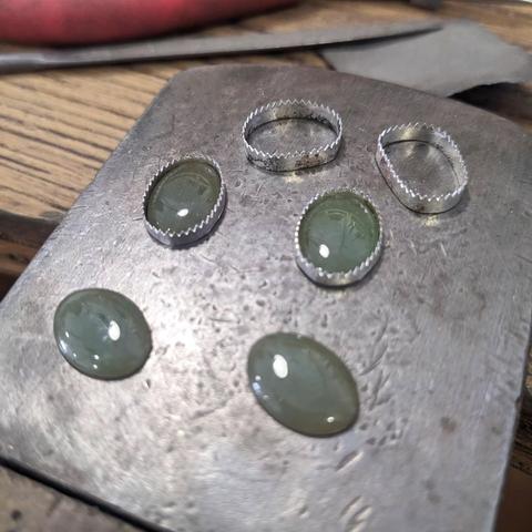 Four jade cabochons on the metal part of a jeweller's peg. Two of the stones are placed in their setting, another two empty settings are nearby.