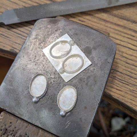Two empty settings with their base in place and roughly cut, another two placed on a piece of sheet of silver ready for the next stage.