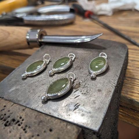 The finished jade cabochons in their settings, on the metal part of a jeweller's peg.