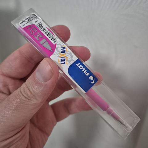 A hand holding a pink refill for a frixion clicker pen.