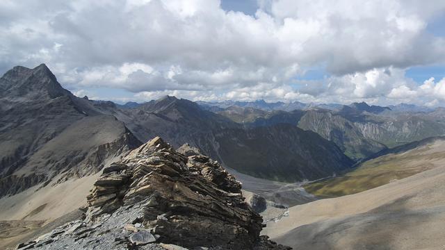 Foto einer Berglandschaft. Blick von einem Gebirgspass auf rund dreitausend Meter über Meer in ein Tal. Im Hintergrund ein Bergpanorama.