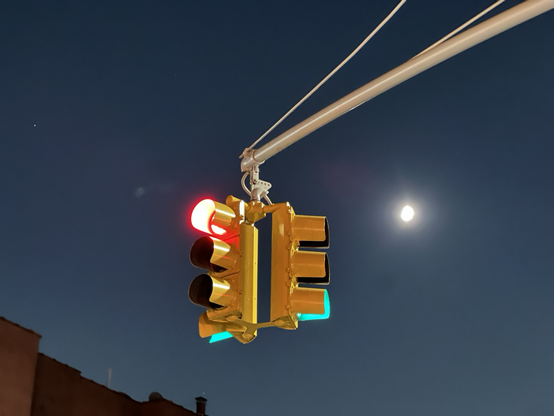 A traffic light showing both red and green colors from two different directions with a night sky in the background.