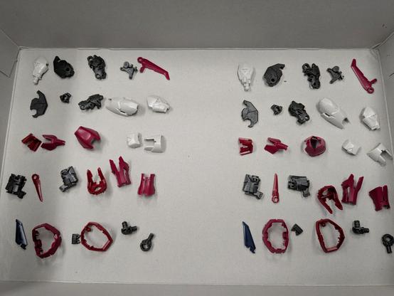 Various gray, red, dark blue, and beige pieces laid out in a roughly organized manner. They are intended to assemble the legs of the RG Gundam Epyon. There are 27 pieces for each leg.