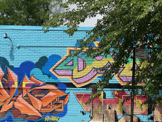 A colorful mural on a brick wall with a green leafy tree on the right