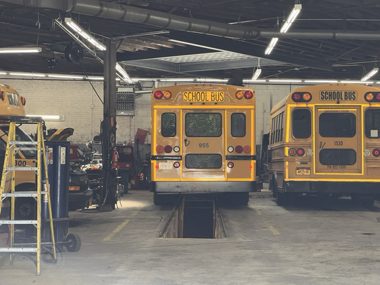 Yellow school buses in a repair garage with a sub repair area below one bus