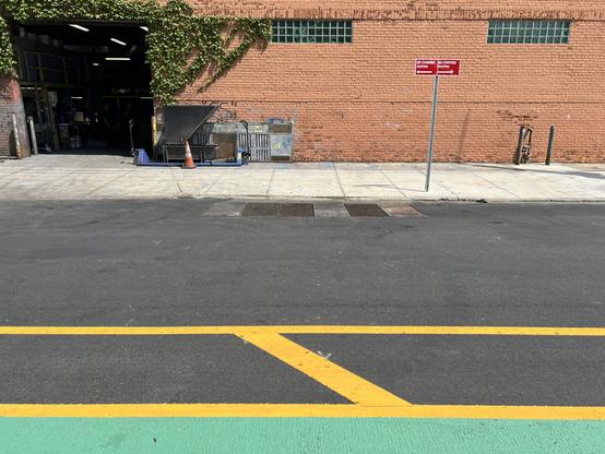 Green from a freshly painted bike lane with yellow border lines in front of a brick industrial building