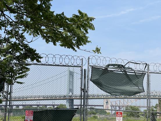 A barbed wire fence with a bridge in the background