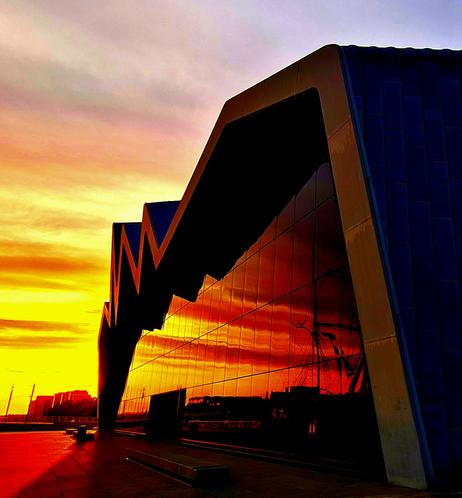 An orange sunset reflected in the glass wall of a modern museum building.
