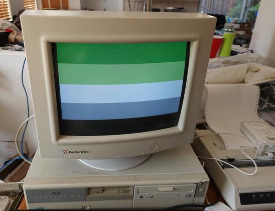 A beige CRT on top of a 90s desktop, displaying the Aromantic pride flag (horizontal stripes of dark green, light green, white, grey, black)