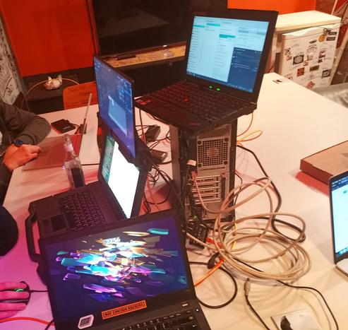 Auf dem Bild ist ein Tisch zusehen drauf stehen mehrere Laptops und ein PC Gehäuse auf dem ein weiter Laptop steht.