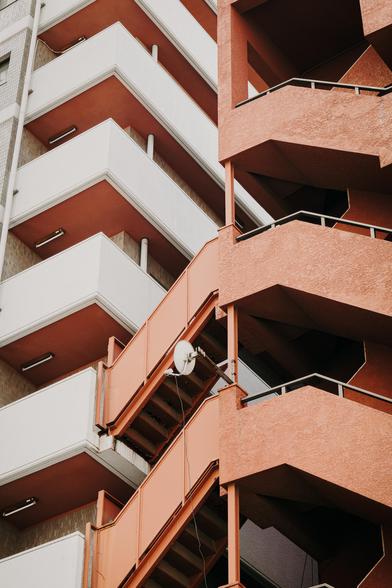 closeup photo of two buildings in Tokyo, one creme white and one brick red. the red building has a satelite dish mounted.