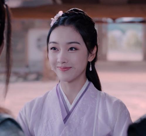 A close-up on Jiang Yanli shown from the shoulders up, garbed in layers of lilac, lavender, and white, smiling happily at her teenage brothers.
