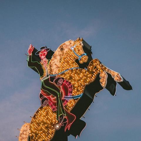 A multi-colored, neon sign of a cowboy on a rearing horse against a blue sky