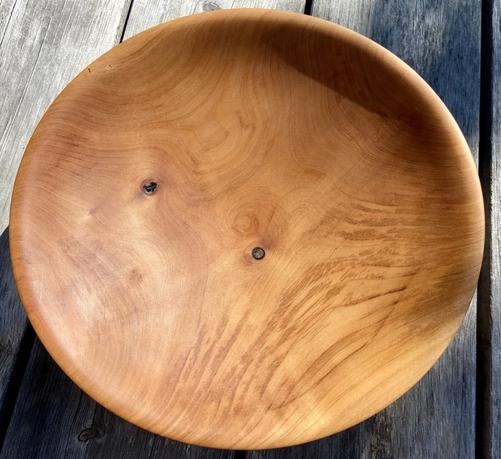 A shallow wooden bowl made from orange-brown wood. There are two small knots in the wood.