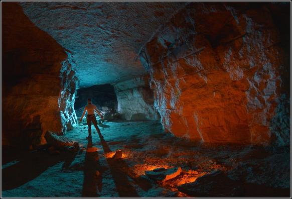 Une galerie souterraine, où de l'éclairage surgit de blocs tombés au sol.
