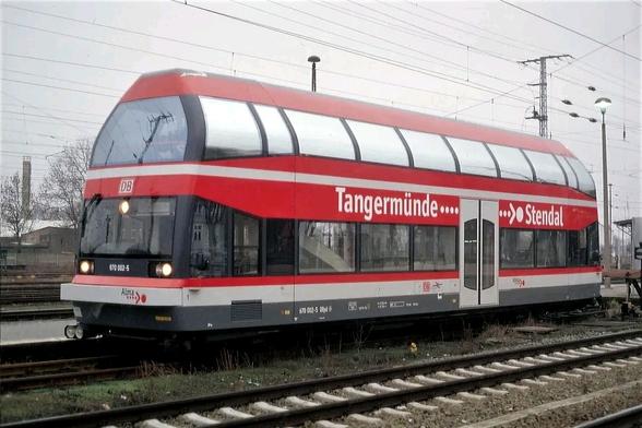 Ein langer roter und weißer Zug mit der Aufschrift „Tangermünde“ und „Stendal“ steht auf einem Bahngleis. Im Hintergrund sind weitere Gleise und ein Teil eines Bahnhofs zu sehen.