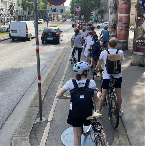 Viele Radlerinnen in einer Reihe auf einen schmalen Radweg, während auf zwei Autofahrspuren gerade mal zwei Autos stehen.