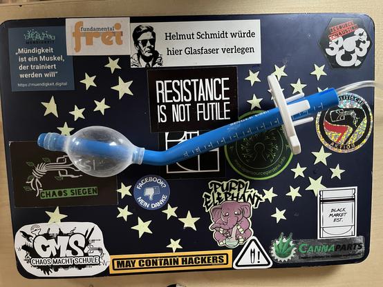 Auf einem 13" MacBook Air mit blauem Cover welches voller, vorwiegend "Hacking" bezogener, Aufkleber ist liegt ein blaues "Teil".

Das "Teil" ist eine 25cm lange Enddarmprothese. Das vordere 12mm dicke Drittel ist ca. 30° abgewinkelt. Die restlichen 2/3 sind 15mm dick. Kurz vor dem Ende ist eine 60mm Scheibe (welche die Tiefe definiert wie weit die Prothese eingeschoben werden muss). Aus dem Ende kommt ein transparenter 3mm dicker Schlauch.
Am vorderen Dritel ist ein kleiner "Luftballon" zu sehen.
Immer wenn die Prothese drinne war - wurde der Ballon mittels des Schlauches aufgeblasen, damit die Prothese sich nicht verschieben kann.

Die Prothese diente dazu den Enddarm aus dem Strahlungsfeld zu drücken, weil er ungünstig lag um eine der Becken-Metastasen optimal Bestrahlen zu können.