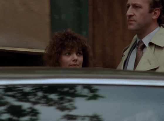 ChatGPT describes the image as "The image depicts a tense, urban setting with two characters, a woman with curly hair and a man in a beige trench coat, standing behind a reflective surface, likely a car. The woman appears attentive or concerned, while the man looks serious and focused, suggesting a moment of confrontation or revelation. The background includes wooden or brick structures, hinting at a city or town environment. The scene likely involves a private exchange or an important conversation, with the characters positioned closely, indicating an intense or significant interaction within a narrative of suspense, crime, or investigation."

BotOfDarkness, version 2.0.23.