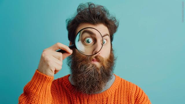 Mann mit Bart schaut durch Lupe und fragt sich, woher das Wort Stau kommt (Foto: Adobe Stock, Anastasiia)