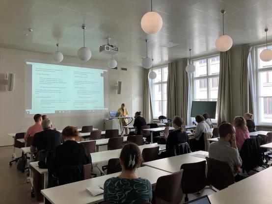 Seminar room with large windows and audience in attendance.