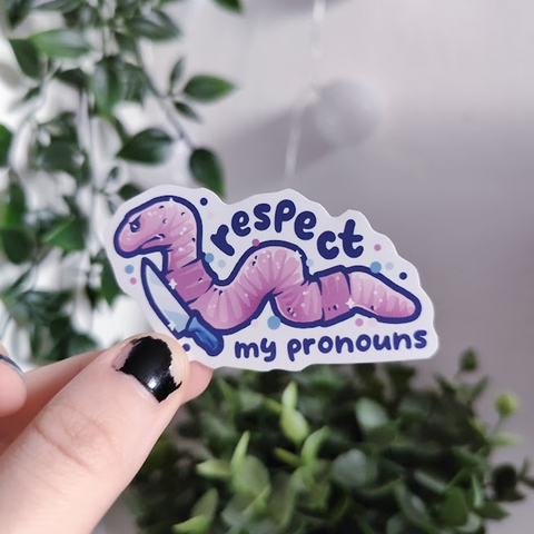 hand holding up a sticker of a pink worm with knife titled "respect my pronouns"