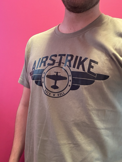 Ein Selfie: Ich trage ein olivgrünes T-Shirt mit dem Wort Airstrike und einer Silhouette eines Propellerflugzeugs, das in einem flügelartigen Logo eingebettet ist. Darunter steht „Rock‘n‘Roll“.