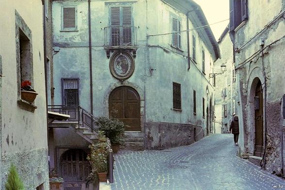 Foto im historischen Ortskern von Ferentino, Lazio, Italien in etwas verblassten Farben. Die Pflasterstraße rechts vorn führt rechts um eine Ecke weiter und biegt auch links hinter einem Treppenübergang ab. Auf den Seiten der Straße historische Wohngebäude, überwiegend in einem etwas lädierten Zustand. Olympus 35SP auf Kodak-Kinofilm.
