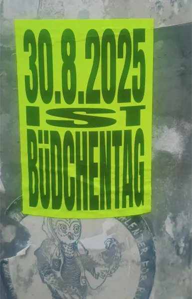 neongelber Sticker auf einem Laternenpfahl mit der Aufschrift mit schwarzer Schrift "30.8.2025 IST BüDCHENTAG" 
unten drunter ein alter, abgeranzter Hermine Sticker mit der Eule