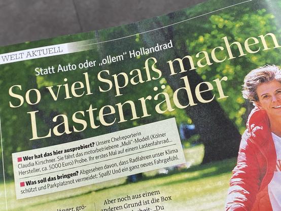 Ausschnitt aus einer Zeitschriftenseite. Am rechten Rand ist eine Frau in einer roten Jacke zu sehen. Die Körperhaltung deutet an, dass sie auf einem Fahrrad sitzt. Vor dem unscharfen Hintergrund, der einen Park oder Wald andeutet, steht:
Statt Auto oder „ollem" Hollandrad
So viel Spaß machen Lastenräder
Wer hat das hier ausprobiert? Unsere Chefreporterin Claudia Kirschner. Sie fährt das motorbetriebene „Muli"-Modell (Kölner Hersteller, ca. 5000 Euro) Probe. Ihr erstes Mal auf einem Lastenfahrrad...
Was soll das bringen? Abgesehen davon, dass Radfahren unser Klima schützt und Parkplatznot vermeidet: Spaß! Und ein ganz neues Fahrgefühl.
Aber noch aus einem anderen Grund ist die (Rest abgeschnitten)