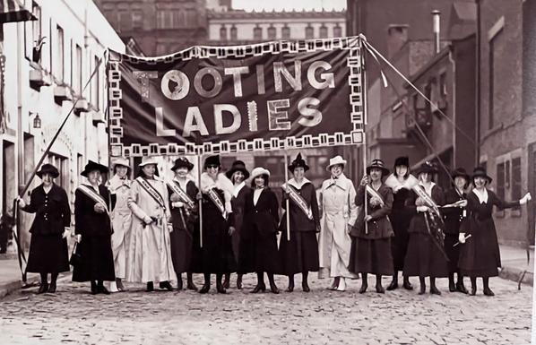 Group of Edwardian in ladies standing under a banner that reads ‘ Tooting ladies’
