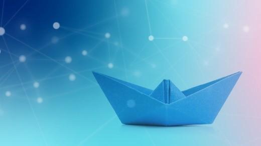 Ein blaues Origami-Schiff vor einem blau-grünem Hintergrund mit Farbverlauf und abstrakten verbundenen weißen Punkten, die einem digitalen Netzwerk ähneln.