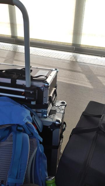 A snapshot of my gig gear, a black hard bag, two rad cases in a trolley and a bit of my blue and grey Fjällräven bergen against a grey sand coloured terminal floor bathing in indirect sunlight that has been filtered by rolling curtains.