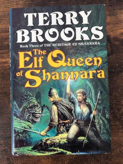 a hardback edition of the Elf Queen of Shannara by Terry Brooks. The cover art depicts an elf lady holds a shining light while an armoured man fights off a demonic spider.