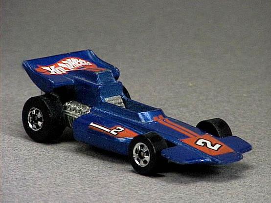 Released in 1985, Metal Flake Blue Malibu Grand Prix of 1985 Hot Wheels with Black Wall wheels. Notes: Grand prix concept racer with exposed metal engine. Available as a Kellogg's promo or at Mattel Toy club. Tampo: Red stripes and white '2' with black outline on front and sides, Hot Wheels logo on rear spoiler. Packaging: 1985 Blister. Metal Body, Metal Base. Made in Malaysia. Scarcity: 3/10