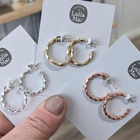 Three pairs of earrings on display cards, held fanned out by a thumb. Each earring is made of twisted square wire, either silver, brass or copper.