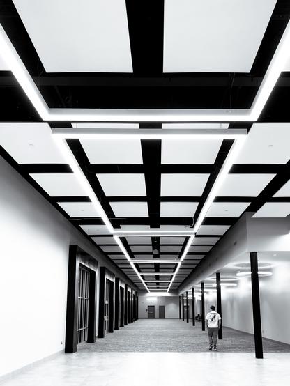A person walks down a modern, geometrically designed hallway with a striking ceiling pattern and bright lighting.
