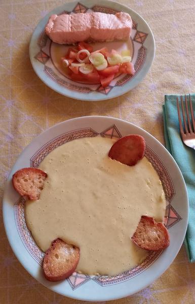 En un plato redondo pequeño un lomo de salmón y un poco de ensalada de tomate y cebolleta.
Un plato hondo con una crema de calabacín y cuatro rebanadas pequeñas de pan frito.
