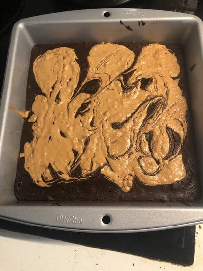 Un gateau au chocolat partielement recouvert de peanut butter dans un moule carré