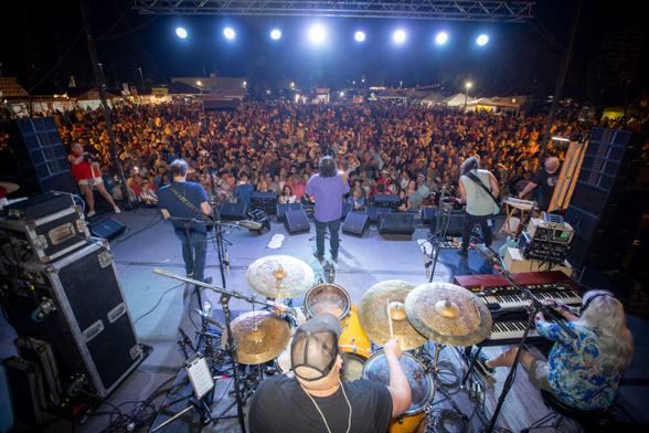 Overhead view of a band playing on a festival stage in front of a large crowd at night.