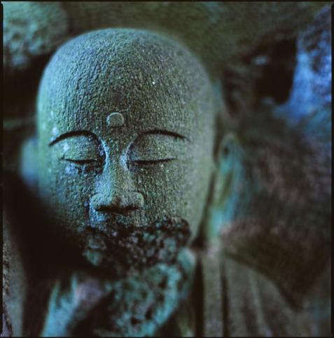 colour photograph of a small buddha, in low light. the colours tend to blue and green. out of focus highlights are almost a neon blue.