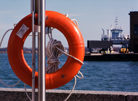 A bright orange life buoy ring, nylon line coiled at the ready, is mounted on an emergency station by the harbourside.