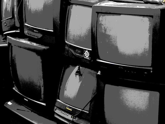 Mostly black and white photo with a reduced color palette (CGA) of a stockpile of an old CRT TVs.